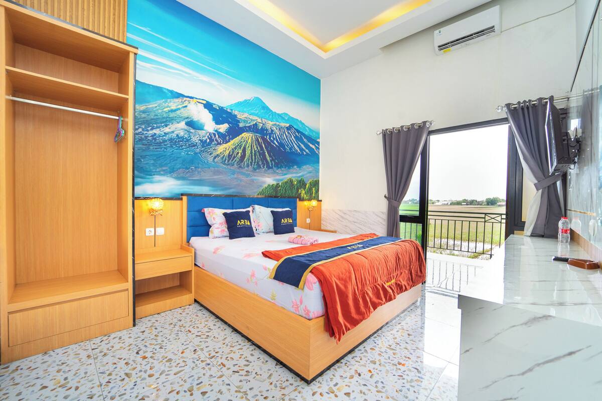 A bedroom with a bed, a wardrobe, a mural, a balcony, and a view of the outdoors.