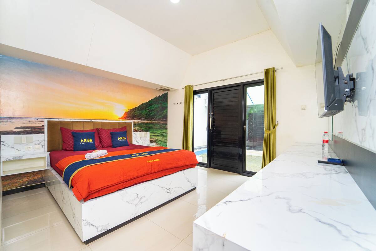 A modern hotel room with a bed, a large window, a TV, and a bathroom door.