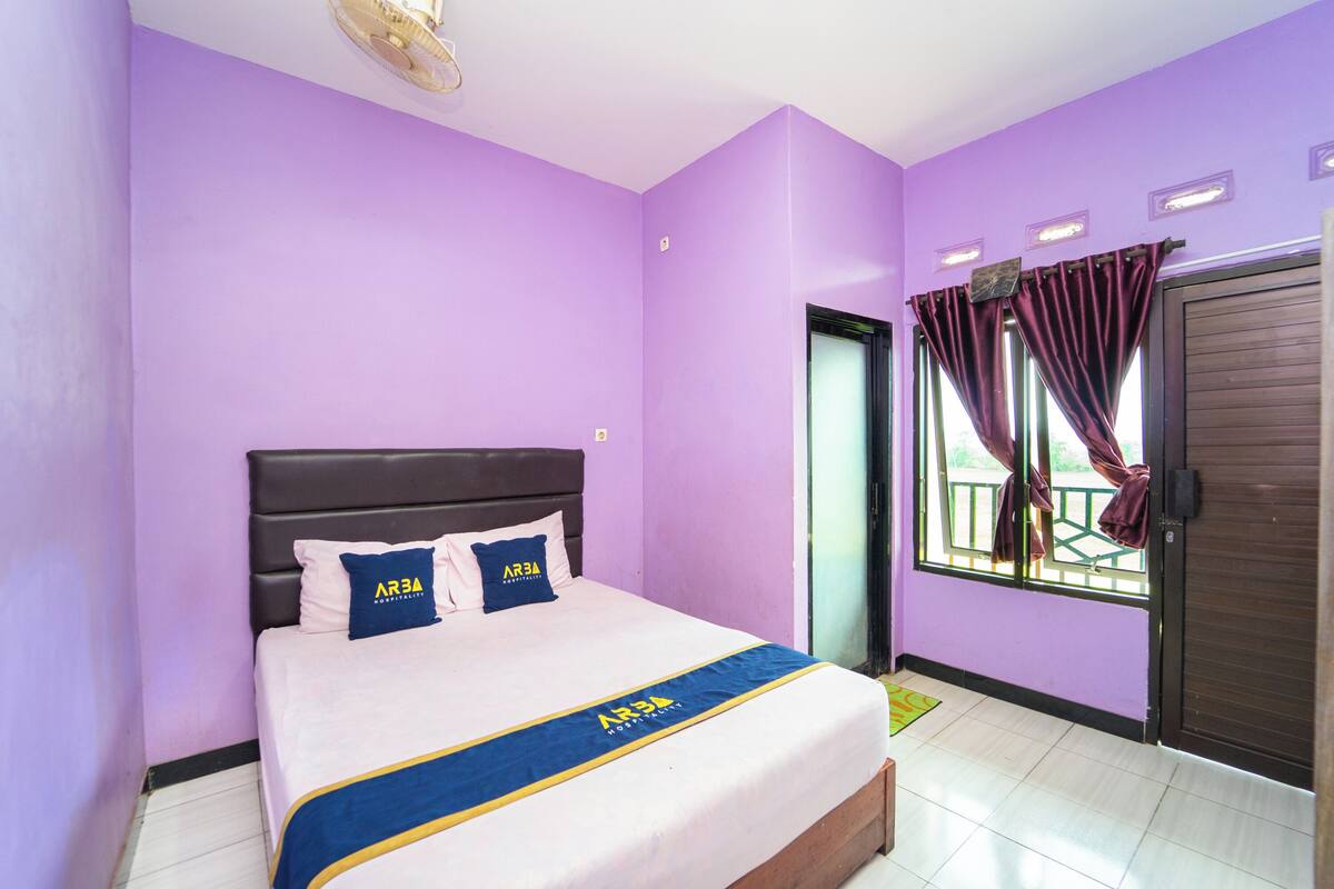 A room with purple walls, a bed with a blue and yellow bedspread, and a window with curtains.