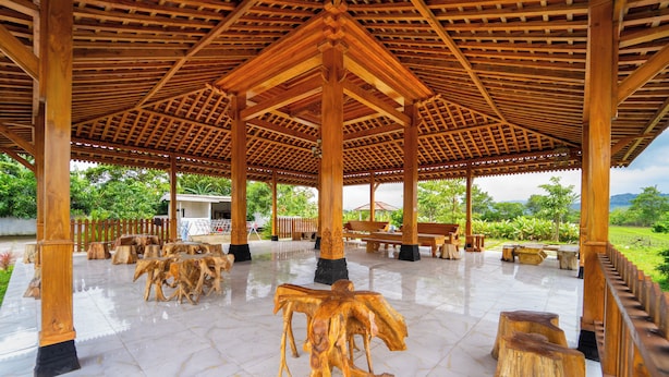 A covered pavilion with a tiled floor, wooden benches, and a central wooden sculpture. - Hotel Tiara by ARBA (Weleri)