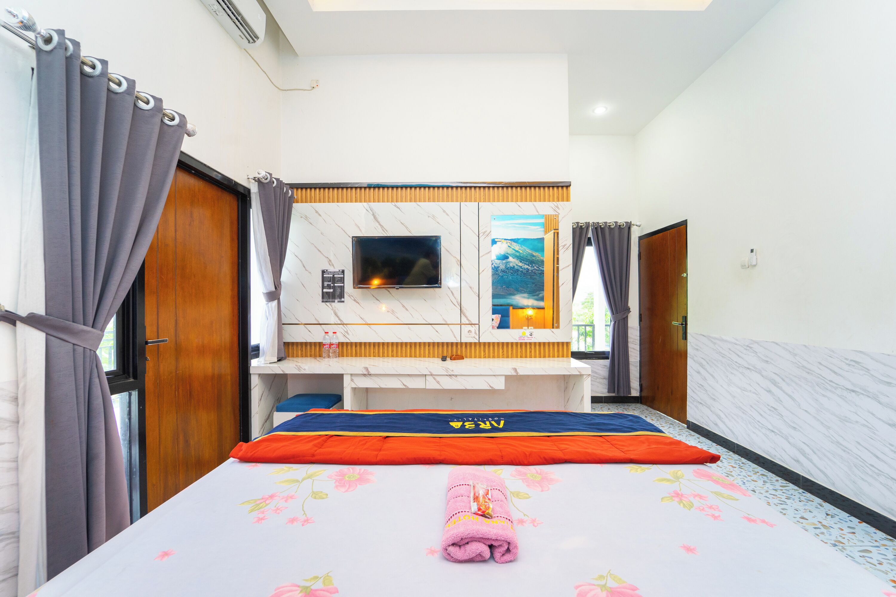 A hotel room with a bed, a TV mounted on the wall, a desk, and a bathroom visible through an open door.