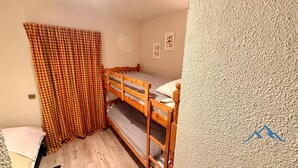 Um quarto pequeno e acolhedor com uma beliche, uma cortina xadrez e algumas decorações nas paredes.