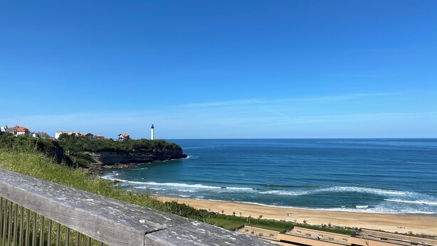 Eine Küstenansicht mit Leuchtturm, Strand und Gebäuden auf einer Klippe.