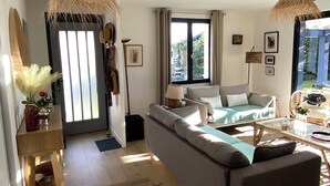 Ein modernes Wohnzimmer mit einer Couch, einem Couchtisch und einem Teppich. Ein Fenster mit Vorhängen, eine Lampe und eine Vase mit Blumen sind ebenfalls zu sehen.
