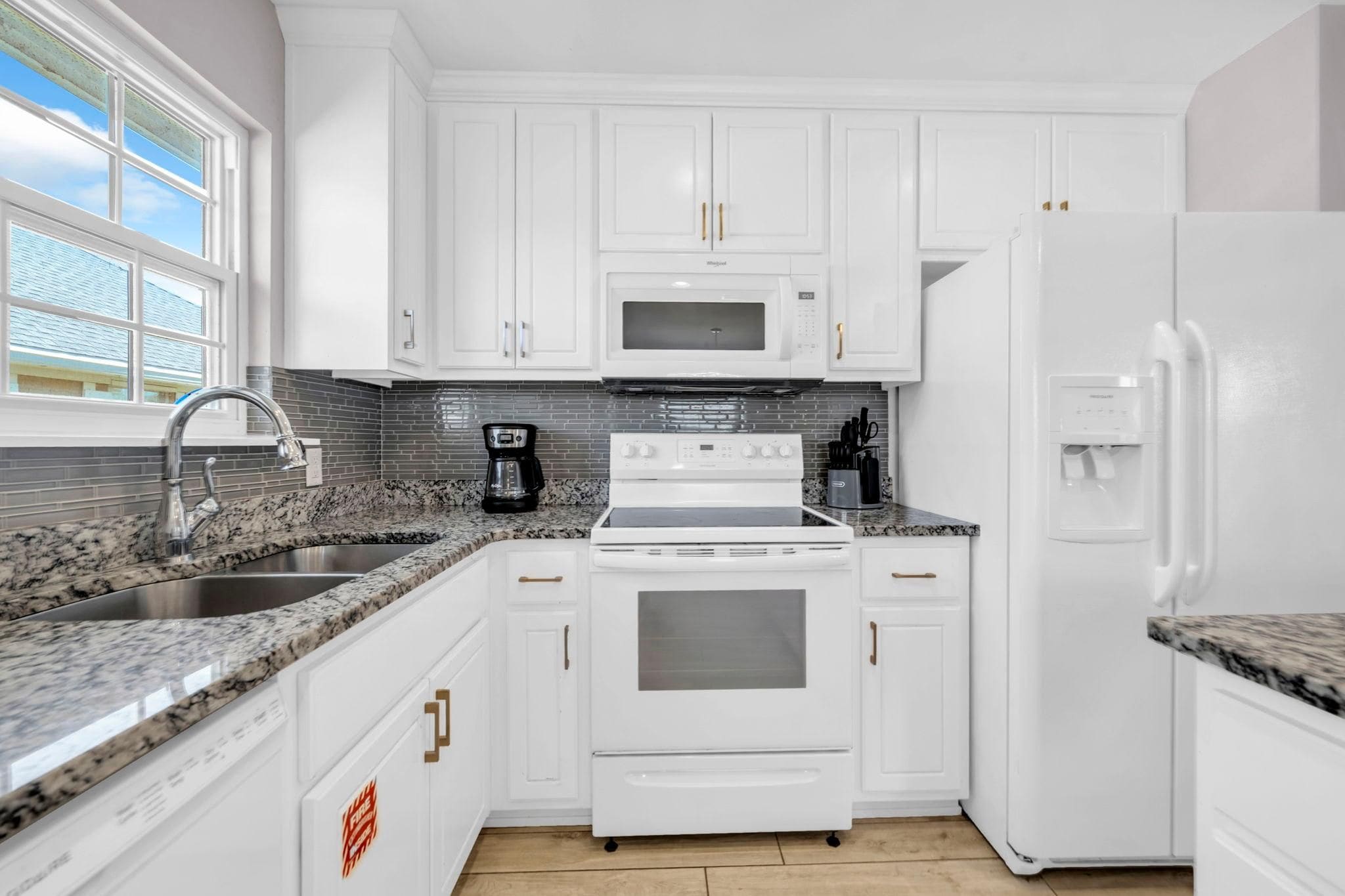 A kitchen with white cabinets, a stainless steel sink, a microwave, a stove, and a refrigerator.