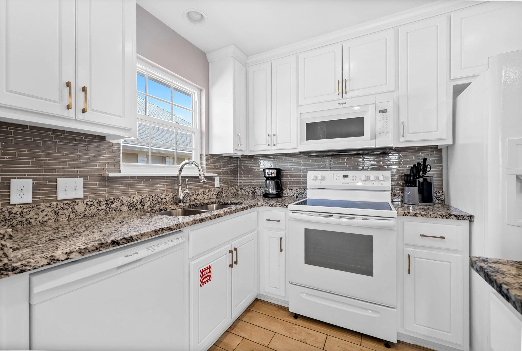 Una cocina moderna con muebles blancos, encimera de granito, microondas integrado, estufa y cafetera.