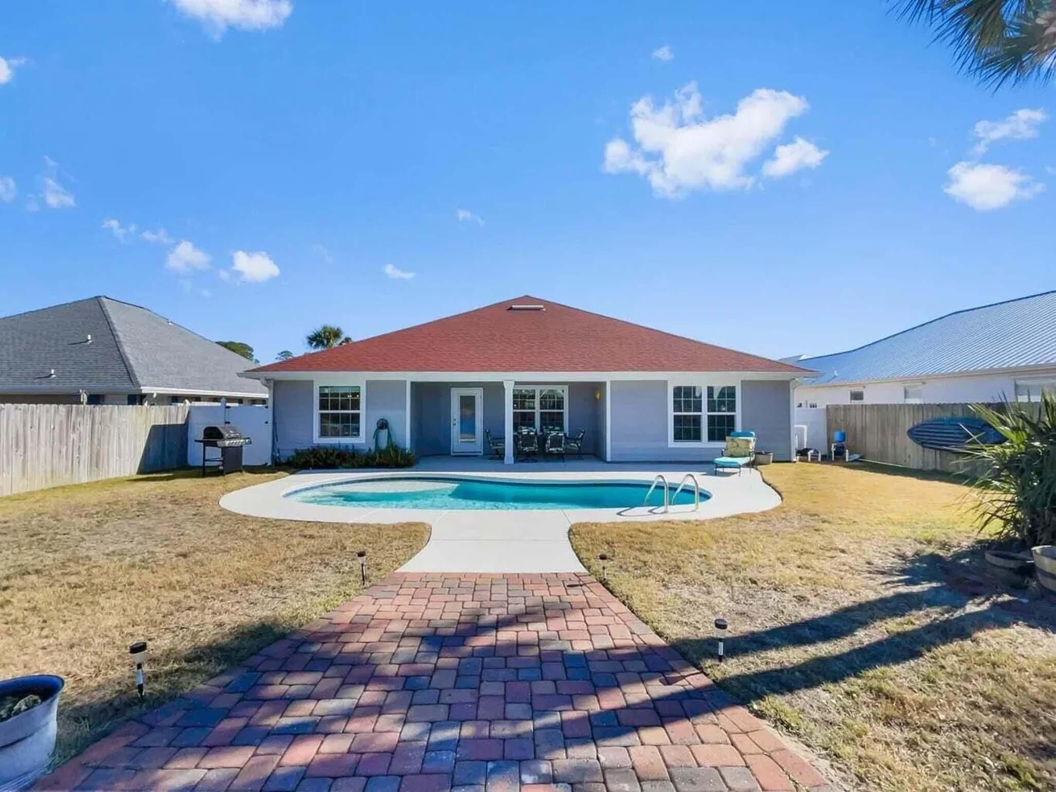 Una casa de dos pisos con piscina, un patio cubierto y un camino de ladrillo que conduce a la piscina.