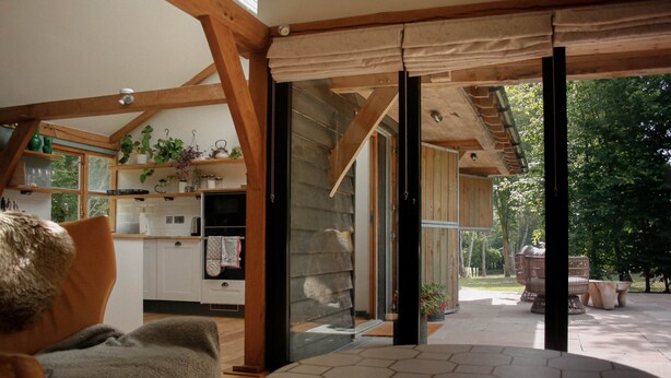 Une cuisine chaleureuse avec des poutres en bois, un coin repas doté d’une table hexagonale et une vue sur un jardin grâce à de grandes portes coulissantes.