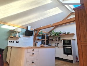 A kitchen with white cabinets, wooden beams, a built-in oven, and a window above the sink. - Kent Family Retreat · Stable + Shepherd's Hut (Cranbrook)