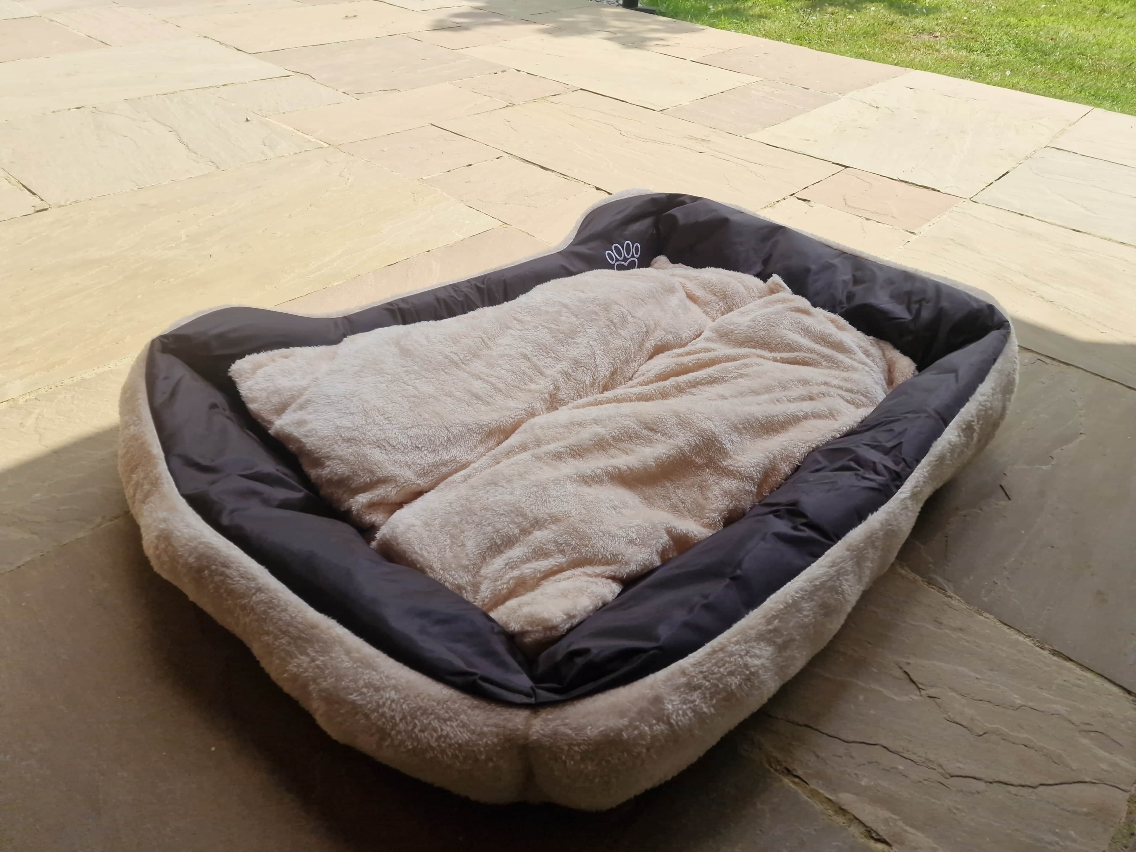 Un panier pour animal de compagnie, avec un intérieur moelleux et un extérieur noir, placé sur une terrasse en pierre.