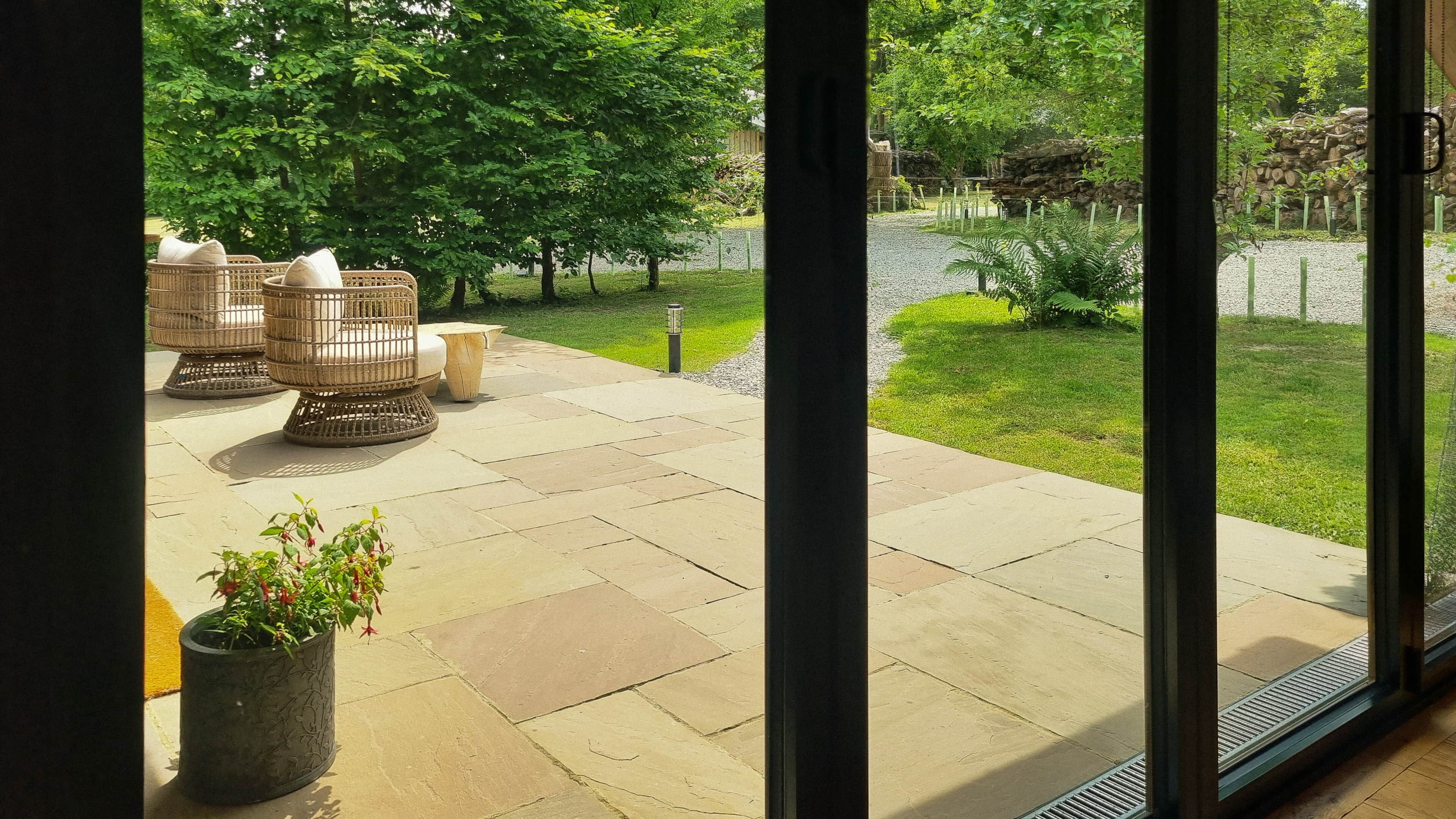Een terras met buitenmeubilair, een kiezelpad en uitzicht op een tuin met bomen en een vijver.