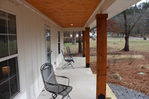 A covered porch with two metal chairs and a table, a wooden ceiling, and a view of a grassy area with trees. - The Alabama Rig @ Mink Creek Boat Ramp-Scottsboro-Guntersville Lake (Scottsboro)