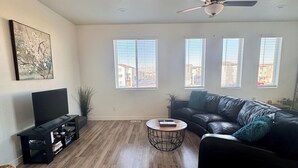 A living room with a black leather sofa, a round coffee table, a TV on a black stand, and a ceiling fan.