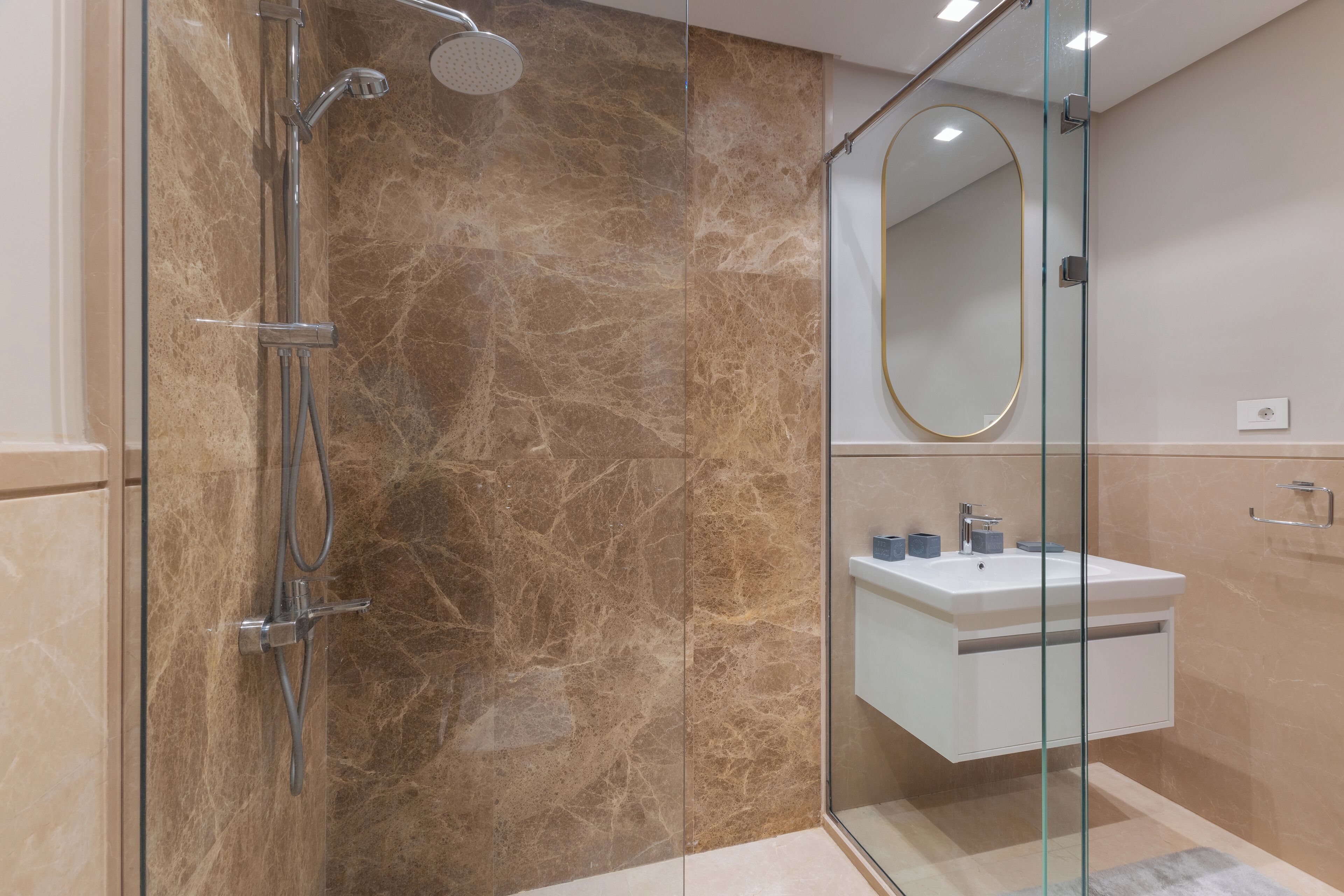 Une salle de bain moderne avec une douche à l’italienne en verre, un lavabo blanc et un grand miroir.