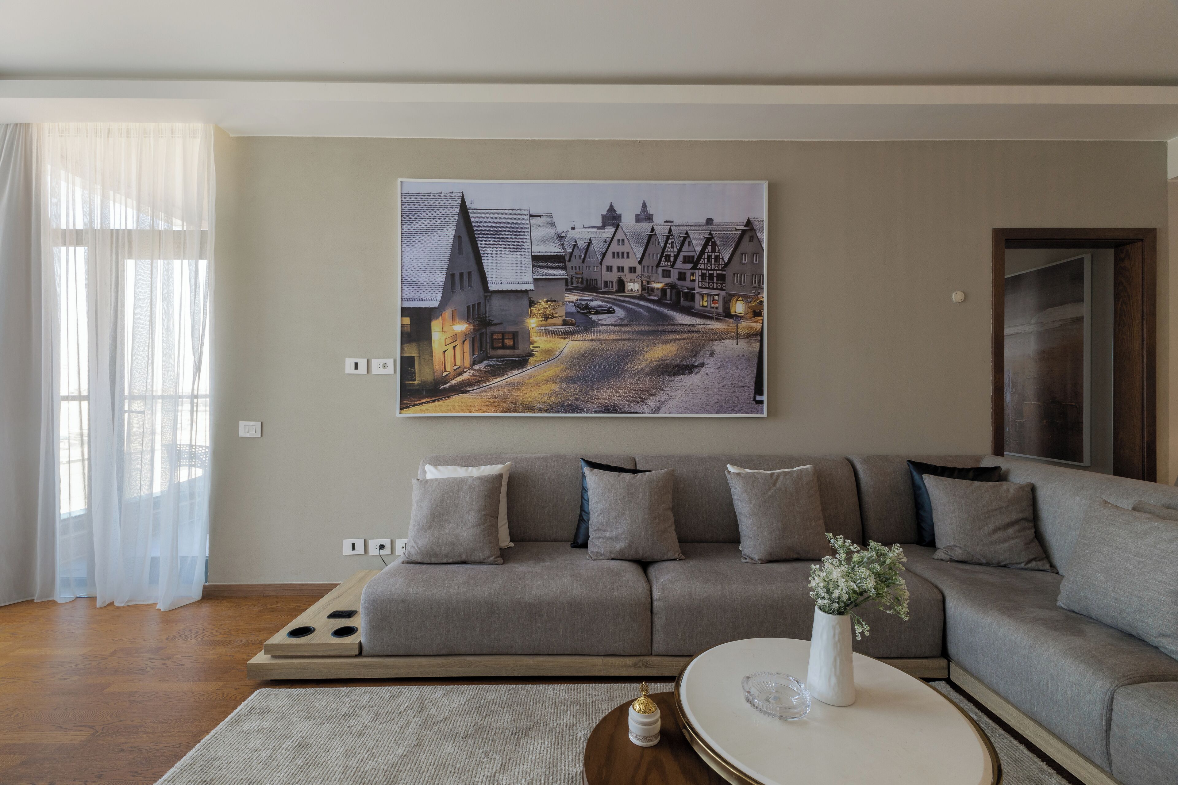 Un soggiorno moderno con un grande quadro che raffigura una scena di strada, un divano grigio e un tavolino rotondo con un vaso.