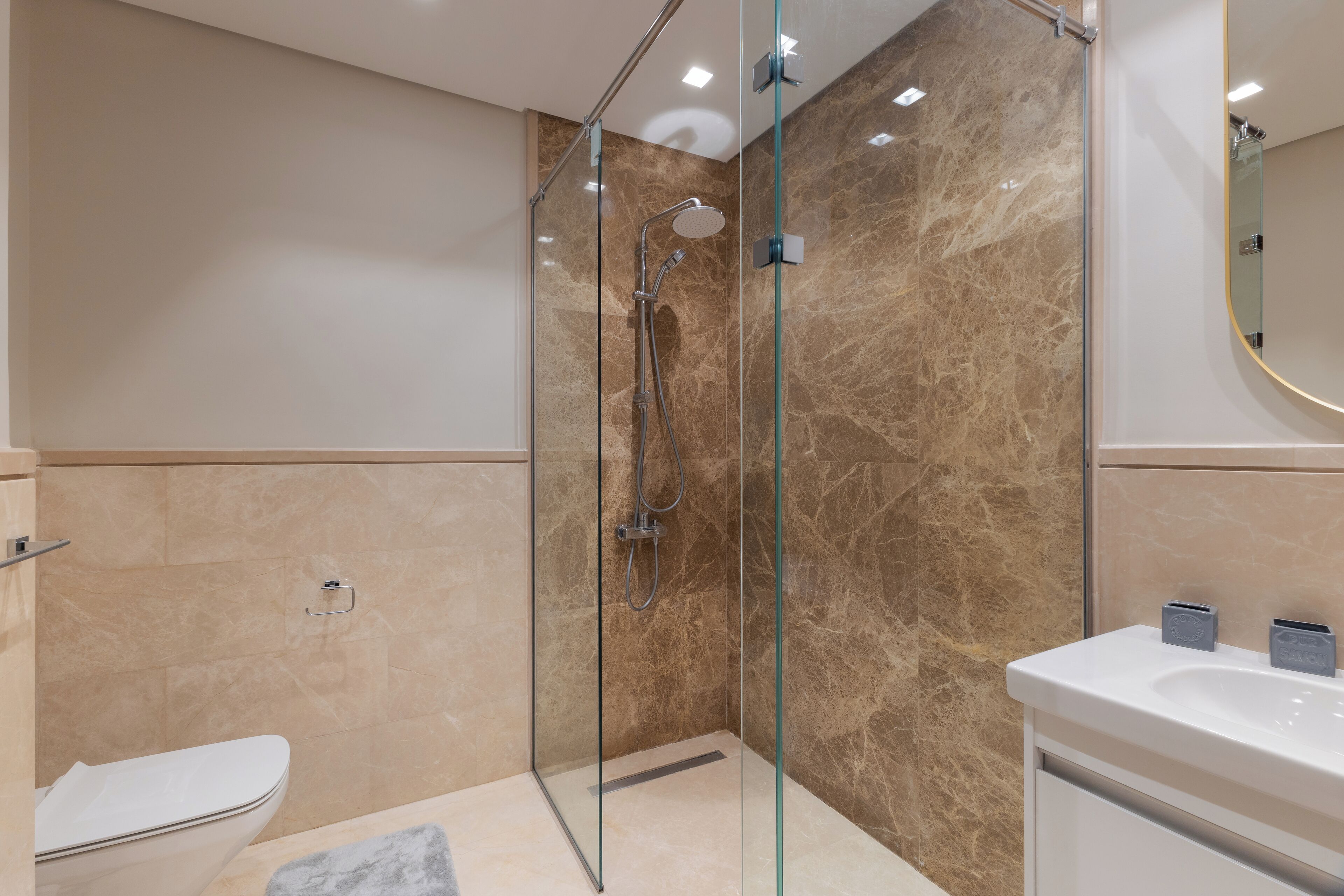 A modern bathroom with a glass-enclosed shower, a white sink, and a marble-tiled wall.