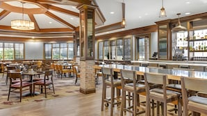 Un vaste espace dédié à la salle à manger, avec des tables et des chaises en bois, un bar proposant un grand choix de boissons, et de grandes fenêtres laissant entrer la lumière naturelle.