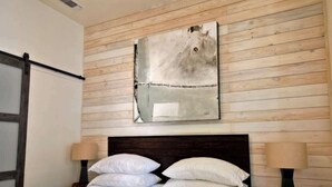 A hotel room with a wooden wall panel design, a large abstract artwork above the bed, and two bedside lamps. - Lodges Combined Suite on the Mason Tx Square (Mason)