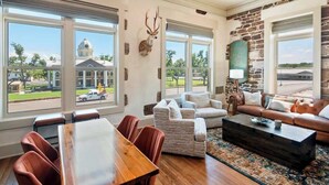 A spacious living room with a large wooden dining table, comfortable seating, and a stone accent wall. - Drifter Suites Combo (Mason)