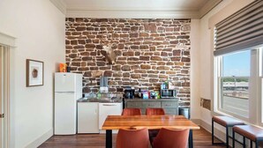 A compact kitchen with a stone wall, a dining table with chairs, and a view of the street through a window. - Drifter Suites Combo (Mason)
