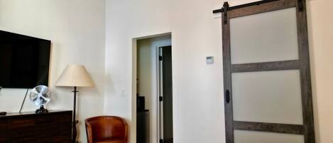 Habitación de hotel con una cama, tocador, lámpara, ventilador, silla y puerta corredera.