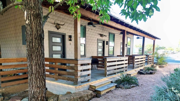 Une cabane rustique dotée d’un porche en bois, d’une porte d’entrée et d’un petit espace extérieur aménagé pour s’asseoir.