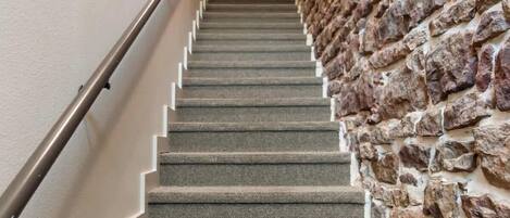 A staircase with a stone wall on one side and a plain wall on the other, leading to a room with a door at the top.