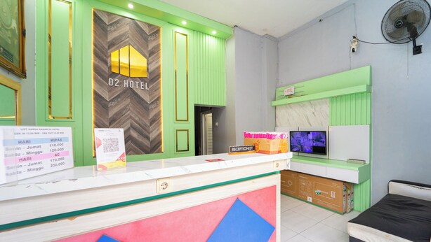 A hotel reception area with a green and white color scheme, a reception desk, a television, and a bed in the background. - Hotel D2 By ARBA (Weleri)