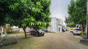 A paved driveway with parked cars and a tree providing shade. - Hotel D2 By ARBA (Weleri)