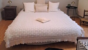Een slaapkamer met een groot bed, een houten hoofdbord, een wandplantenarrangement, een klein nachtkastje met een lamp en een radiator.