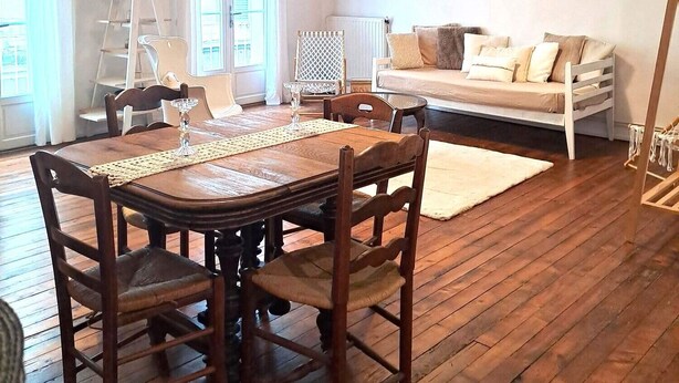 Een ruime kamer met een houten eettafel, stoelen, een bank en een ladder tegen de muur.