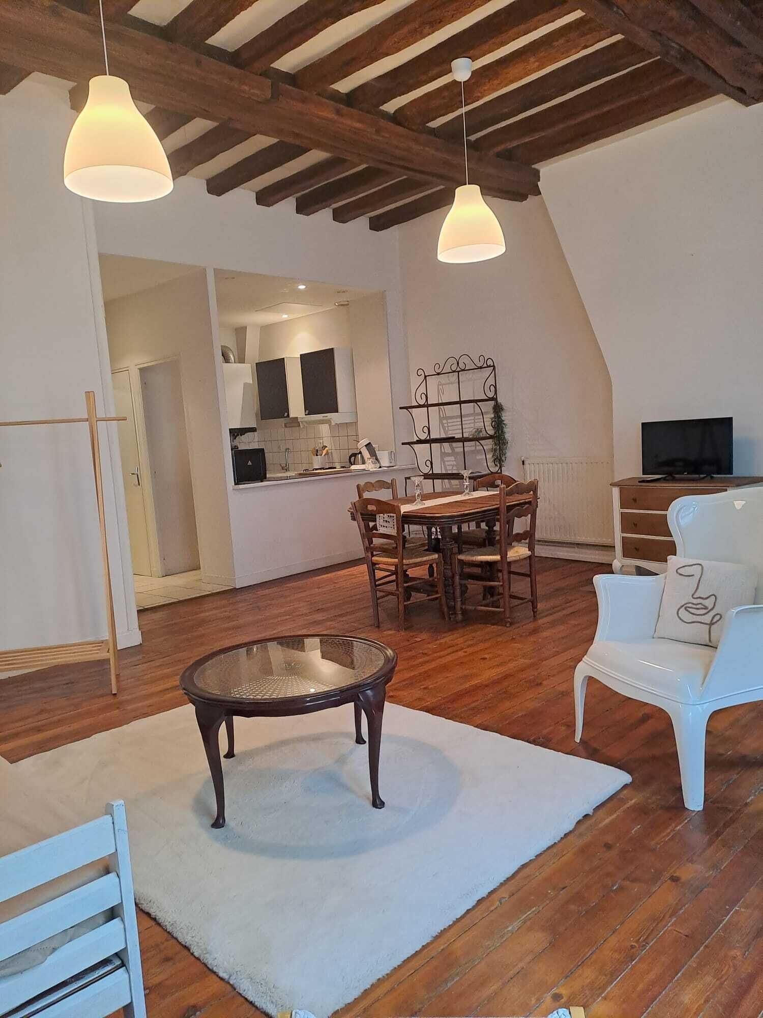 Amplia sala de estar con techo de madera, una mesa de comedor con sillas, una mesa de centro de vidrio y un sillón blanco.