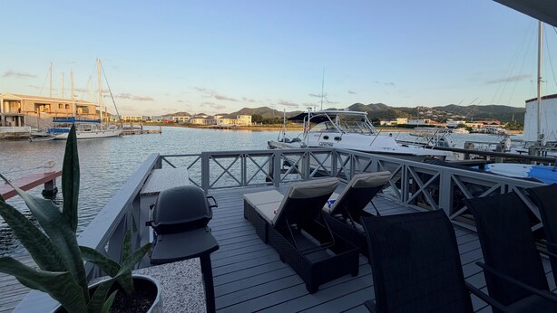 A deck with lounge chairs and a potted plant, overlooking a marina with boats and houses in the background.