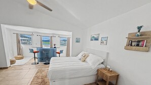 A bedroom with a bed, a desk, two chairs, a rug, and a shelf with books.