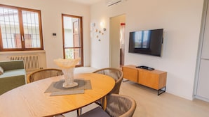 Una sala de estar moderna con una mesa de comedor de madera, sillas de mimbre, un televisor de pantalla plana y un pequeño mueble de madera.