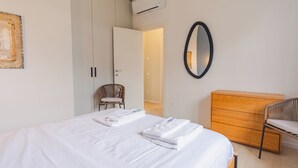 Un dormitorio con una cama, un aparador de madera, una silla de mimbre y un espejo en la pared.