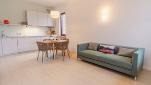 Una cocina moderna con armarios blancos, una mesa de comedor con sillas de mimbre y un sofá verde con cojines decorativos.