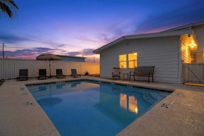 Une piscine rectangulaire, bordée d’une terrasse carrelée, entourée de chaises longues et agrémentée d’un petit espace patio avec une table et des chaises.