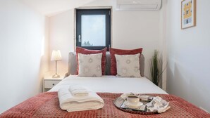 Hotelkamer met een bed, raam, airconditioning, nachtkastje, lamp, dienblad met een kop koffie en een boek.