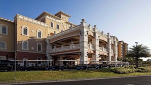 Un hotel grande con una entrada imponente, varios balcones y una zona cubierta con carros de golf.