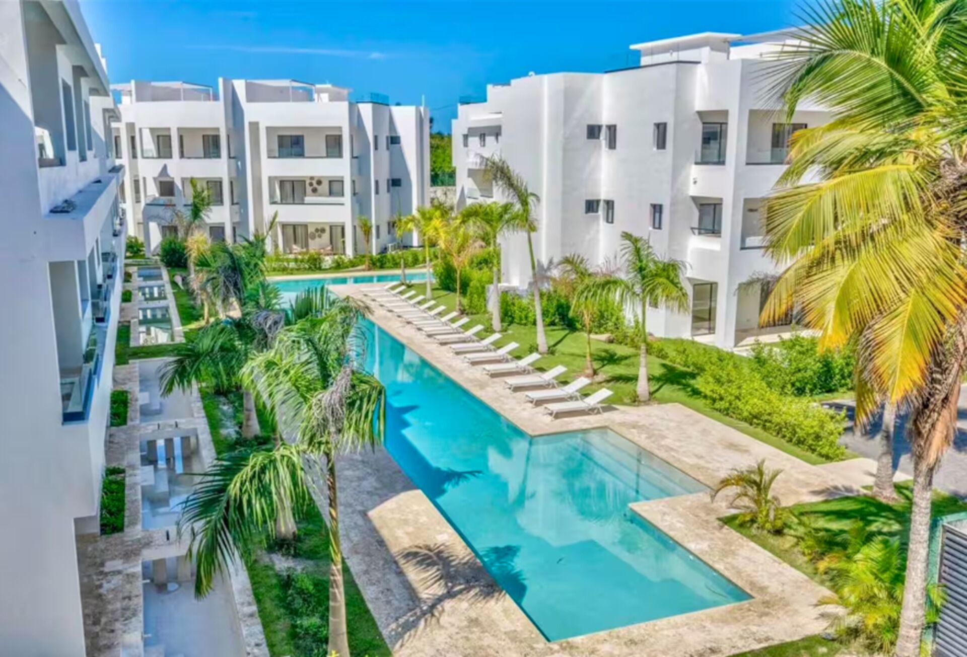 Ein modernes Resort mit einem zentral gelegenen Schwimmbad, umgeben von Liegestühlen und Palmen.