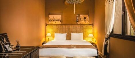 A hotel room with a large bed, two bedside lamps, a decorative ceiling light, and two ottomans.