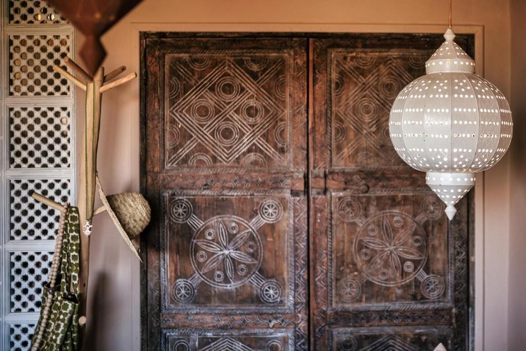 A wooden door with intricate carvings and a hanging white lantern.