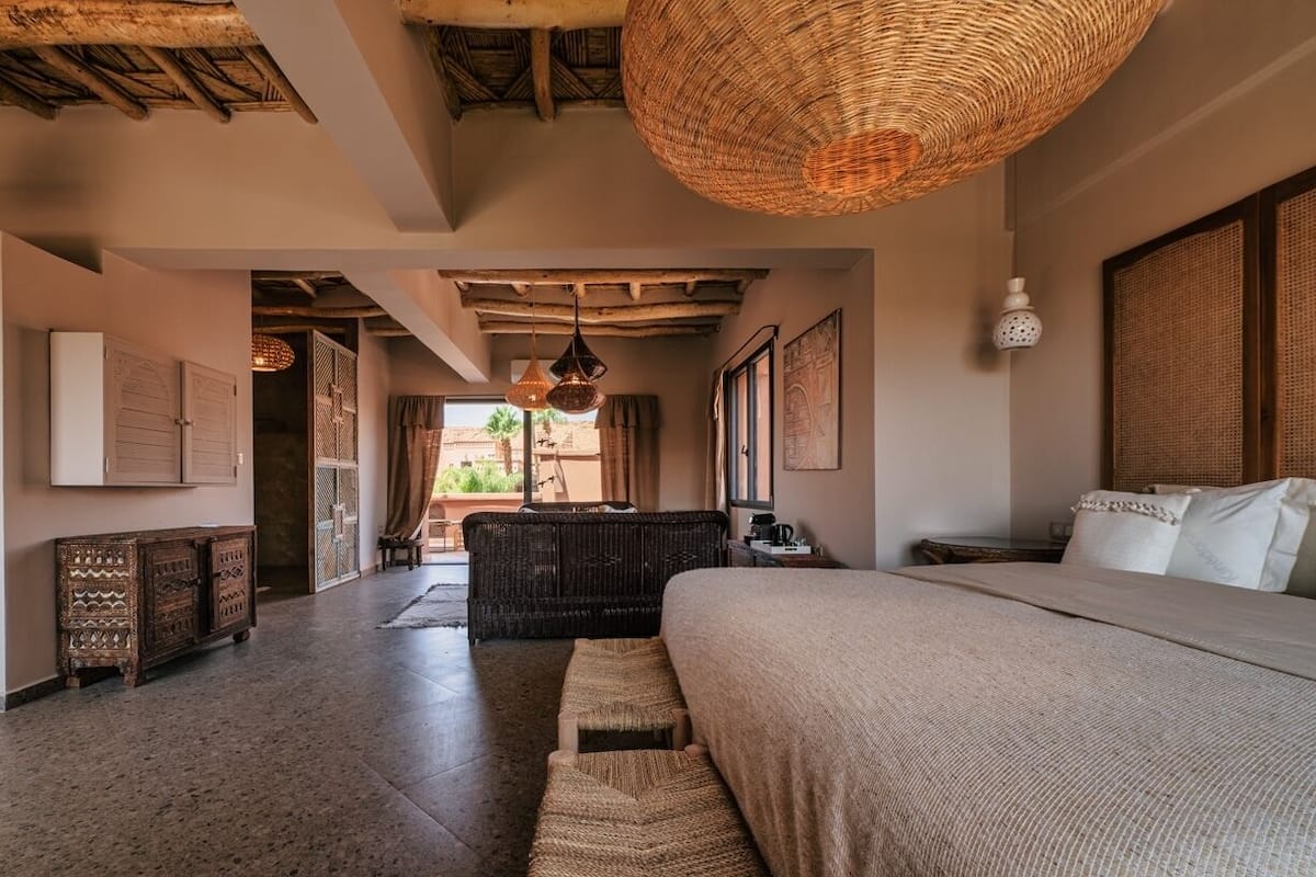 A spacious bedroom with a large bed, a wicker ceiling light, and a view of the outdoors.