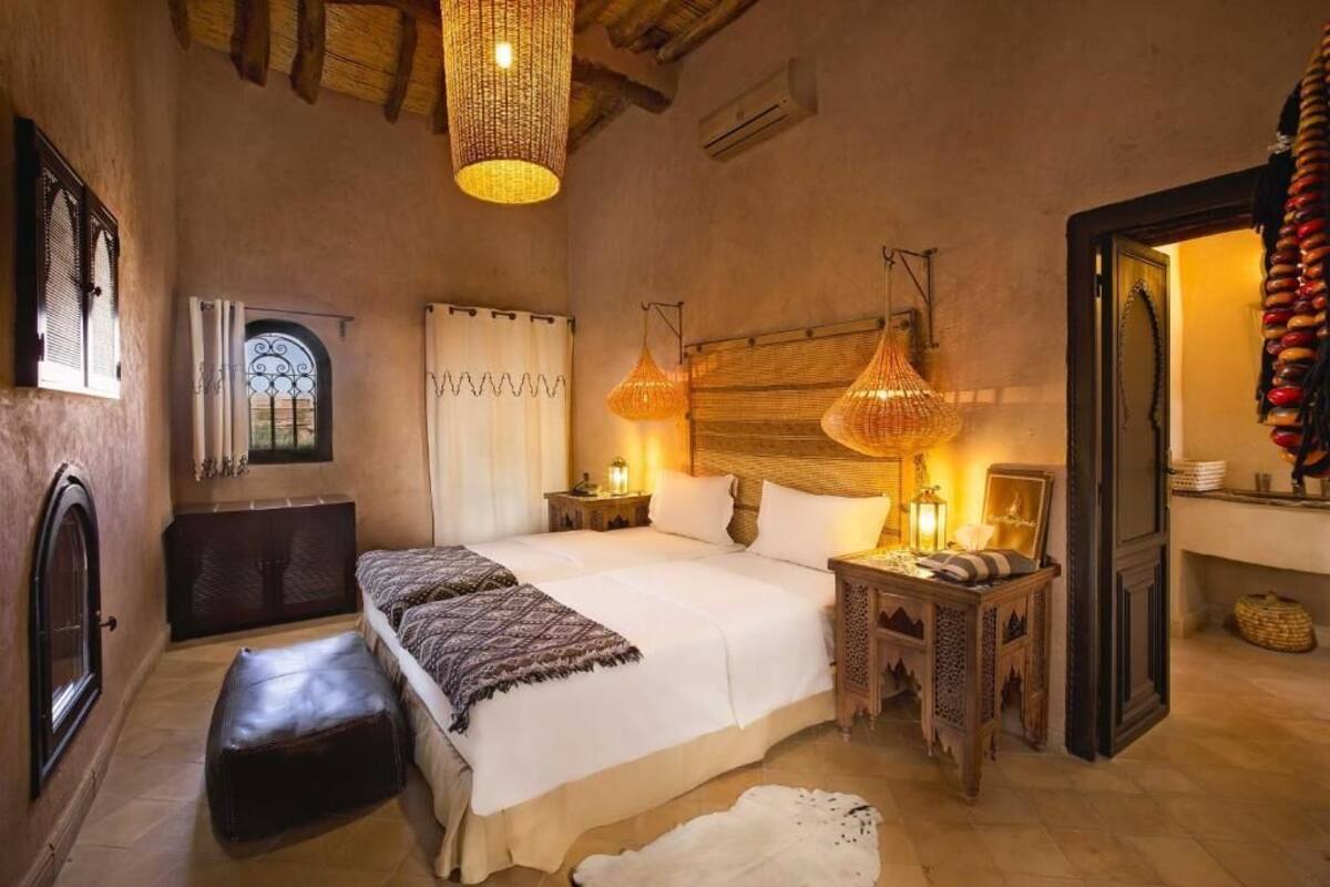 A cozy bedroom with a large bed, two bedside tables, a small bench, and a woven ceiling light fixture.