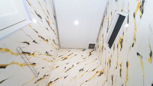 A room with a white marble floor featuring black and gold streaks, a white door, and a vent on the wall. - Hotel Panorama Batang By ARBA (Banyuputih)