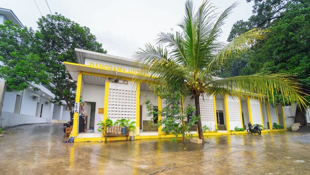 A building with a yellow and white facade, a palm tree, and a parked motorcycle. - Hotel Panorama Batang By ARBA (Banyuputih)