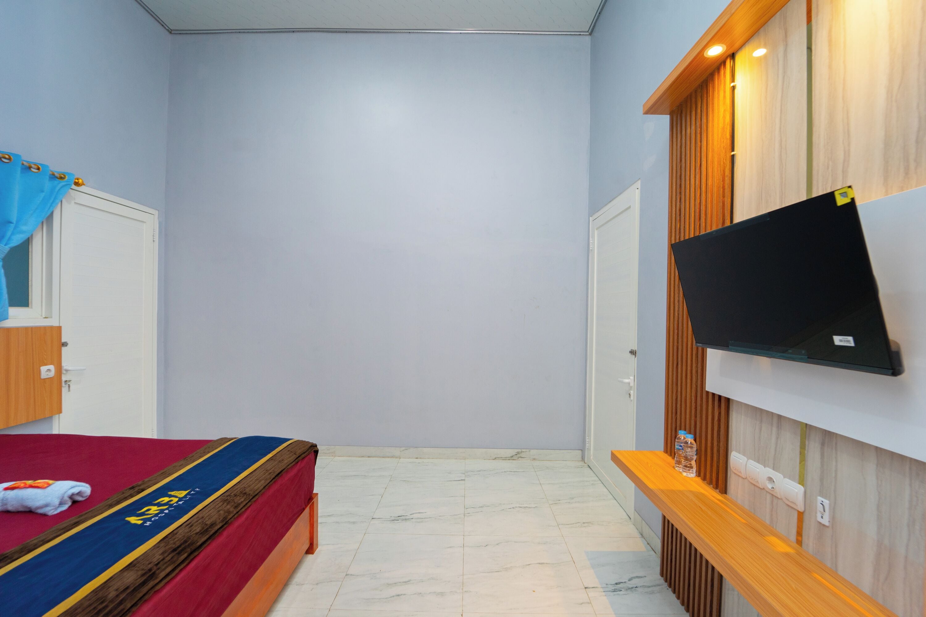 A hotel room with a bed, a TV mounted on the wall, a wooden bench, and a water bottle on the bench.
