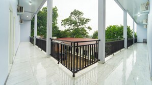A spacious balcony with a tiled floor and a metal railing, overlooking a lush green area. - Hotel Panorama Batang By ARBA (Banyuputih)