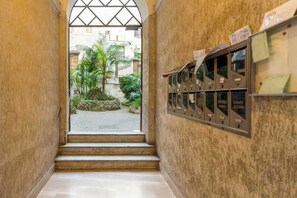 A corridor with a metal mail slot on the right wall and a view of a courtyard with plants and buildings outside. - ZUCCHELLI ROMAN RESIDENCE (Roma)